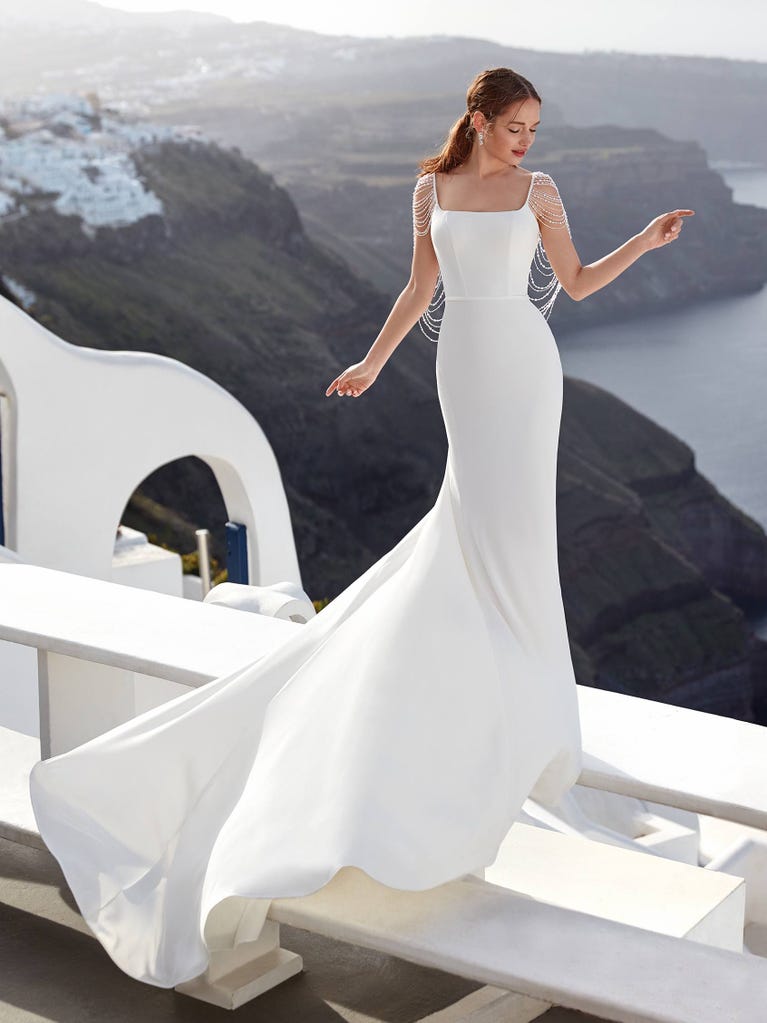 Flared wedding dress with crepe skirt and a tulle cape embroidered with silver beads. The three-dimensional flowers and minimalist, geometric superimpositions of fabrics create a contemporary, unique look for brides who want to surprise.