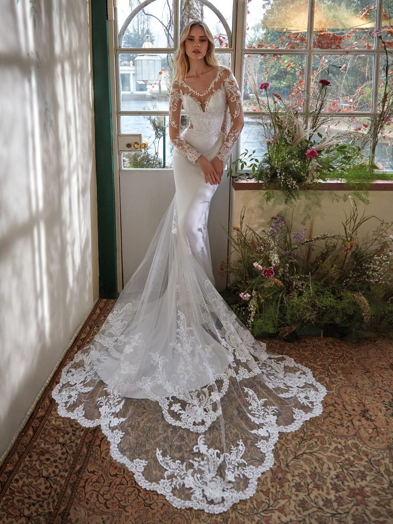 Flared wedding dress with crepe skirt and a tulle cape embroidered with silver beads. The three-dimensional flowers and minimalist, geometric superimpositions of fabrics create a contemporary, unique look for brides who want to surprise.