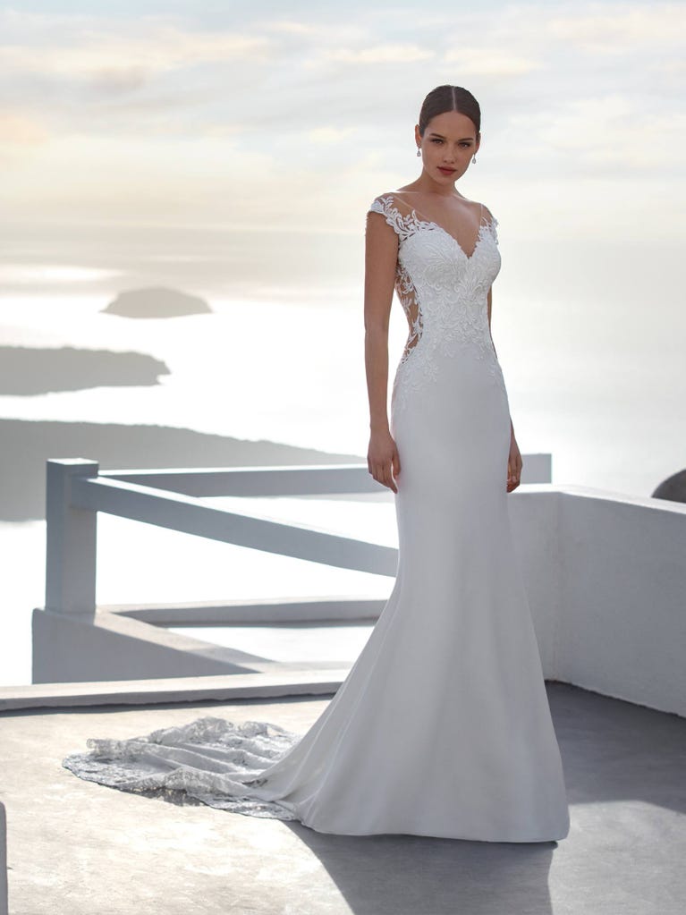 Flared wedding dress with crepe skirt and a tulle cape embroidered with silver beads. The three-dimensional flowers and minimalist, geometric superimpositions of fabrics create a contemporary, unique look for brides who want to surprise.