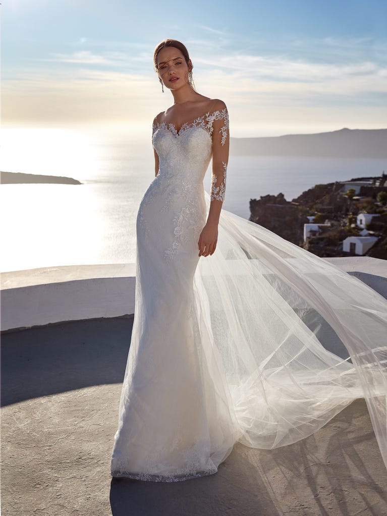 Flared wedding dress with crepe skirt and a tulle cape embroidered with silver beads. The three-dimensional flowers and minimalist, geometric superimpositions of fabrics create a contemporary, unique look for brides who want to surprise.
