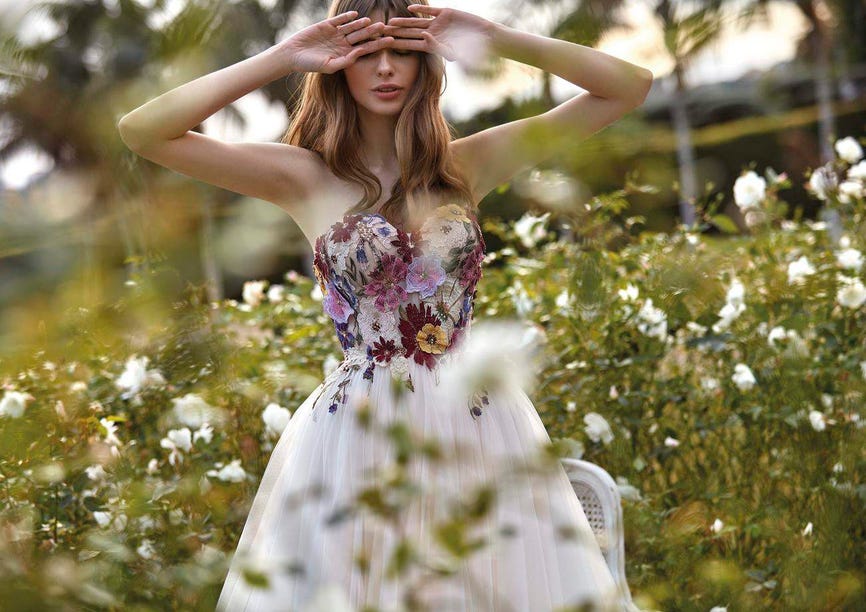 Une jeune femme au milieu d’un champ, vêtue d’une robe de mariée bustier dotée de fleurs en dentelle colorées sur le haut