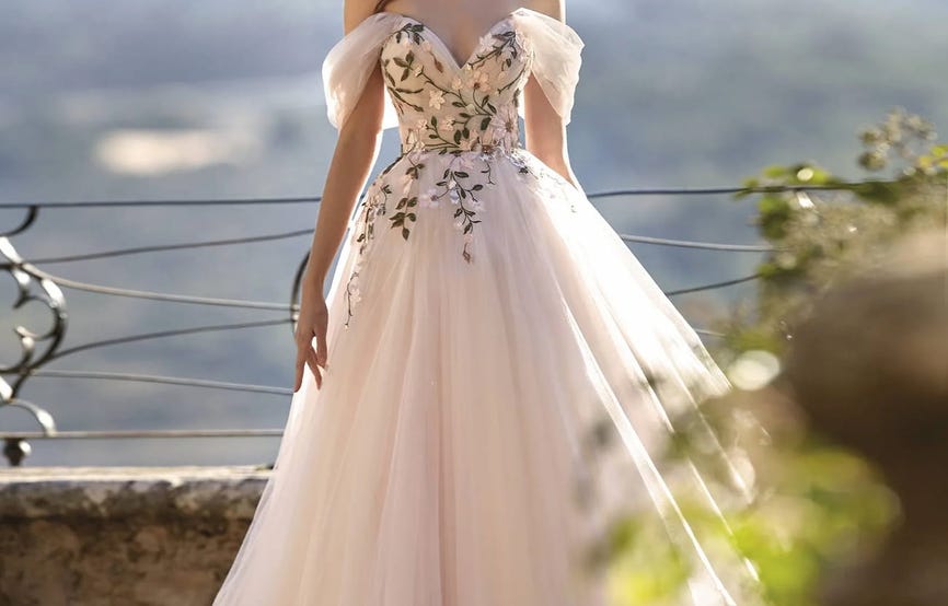 Modella con abito da sposa romantico rosa a principessa con scollo a cuore, spalle scoperte e dettagli floreali sul corpetto.