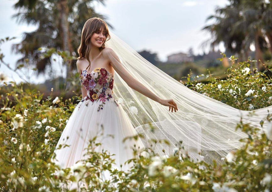 Une belle jeune femme vêtue d’une magnifique robe de mariée champêtre rehaussée de fleurs en dentelle colorées sur le buste.