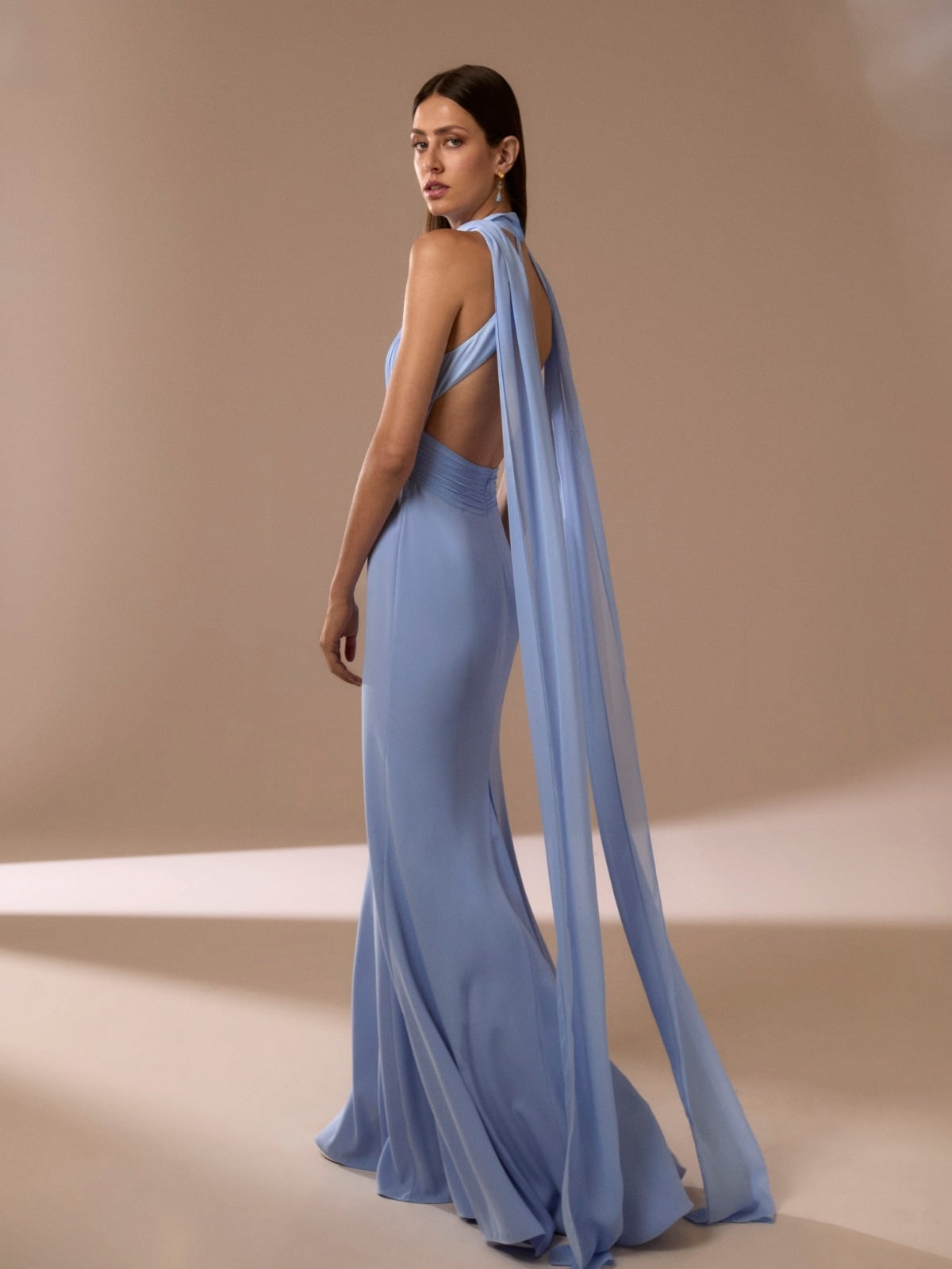 Une demoiselle portant une robe invitée de mariage élégante en tulle mauve, accroupie au niveau d’une grande fenêtre.