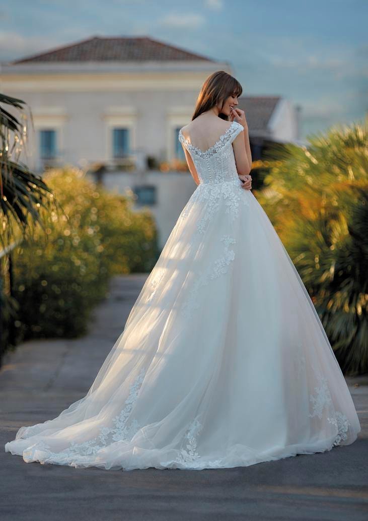 Donna di spalle in piazza con un abito da sposa a principessa lungo e ricamato e con spalle cadenti.