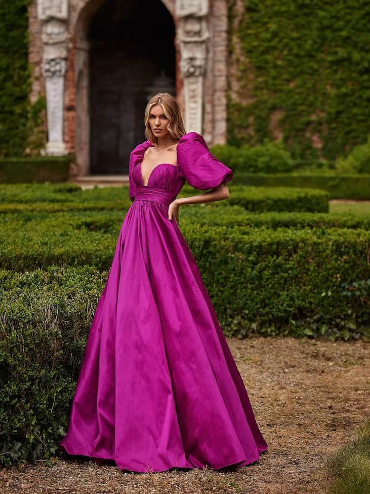 Une jeune demoiselle vêtue d’une robe d’invitée de mariage longue fuchsia, dotée de manches bouffantes à couper le souffle