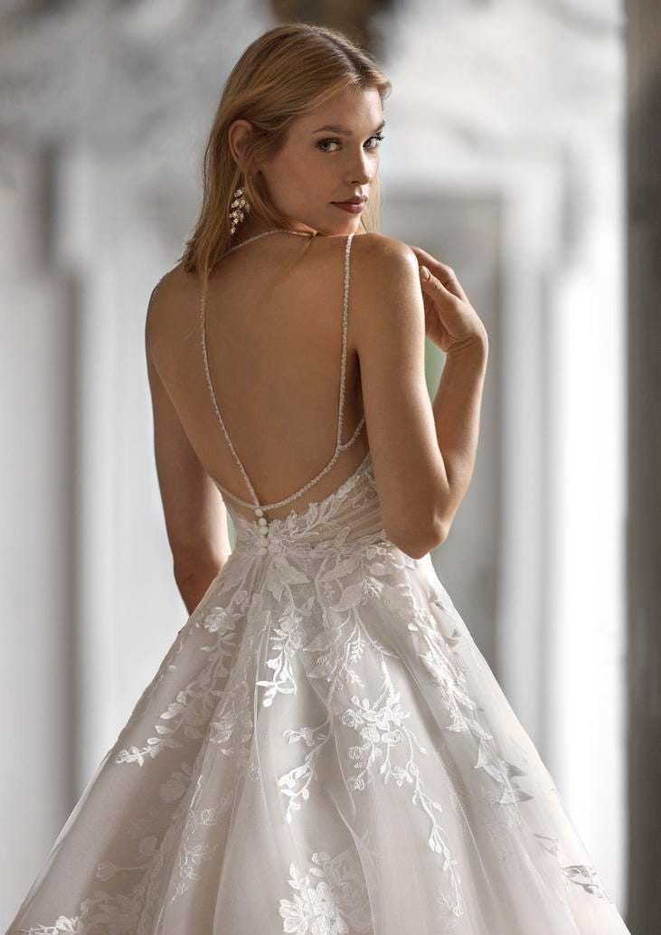 Donna di spalle che indossa un vestito da sposa con schiena scoperta e spalline. Ha orecchini pendenti e un makeup naturale