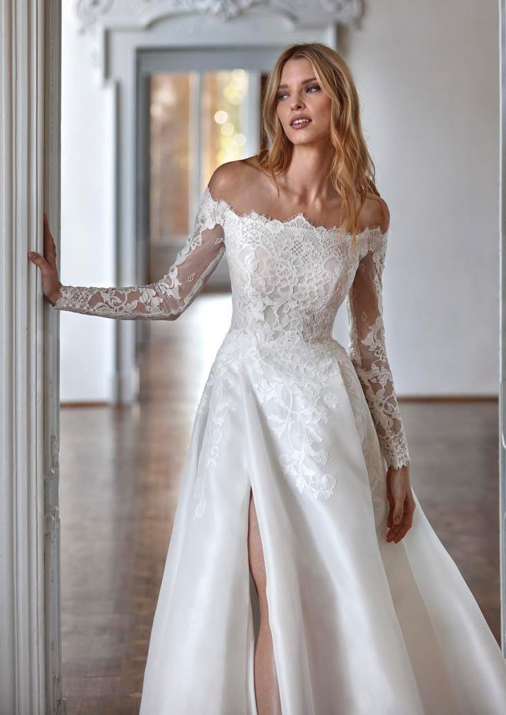 Sposa con vestito a principessa a maniche lunghe, corpetto interamente in pizzo e gonna in mikado con spacco.