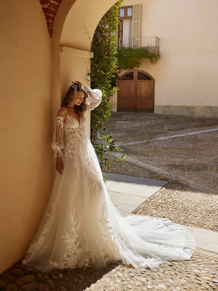 Abito da Sposa Romantico a Trapezio Modella con abito da sposa a trapezio ricamato con maniche lunghe, spalle scoperte e scollatura a cuore.